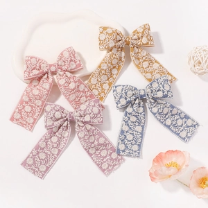 Détail de quatre barrettes nœuds faites main avec de délicates broderies de marguerites blanches