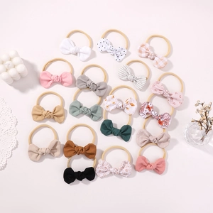 Flat lay of 15 infant bow headbands in various patterns and soft colors for baby girls