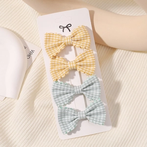 Close-up of four plaid bow hair clips in yellow and green on a white display card