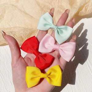 Detail showing four colorful grosgrain ribbon hair bows held by hand for size reference