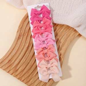 Dettaglio di cinque fiocchi per capelli in tessuto a nido d'ape in toni rosa e beige