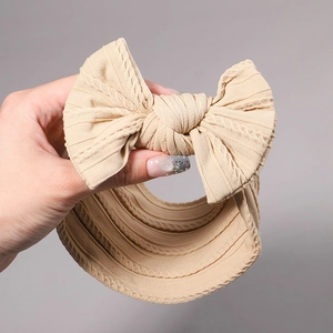 Detail of a beige knit bow headband for infants showing soft elastic spiral texture
