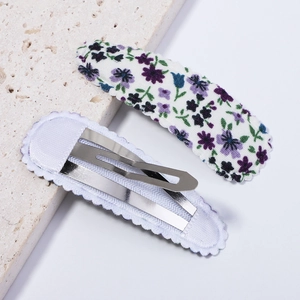 Détail de pinces à cheveux en tissu floral montrant l'imprimé et la structure métallique