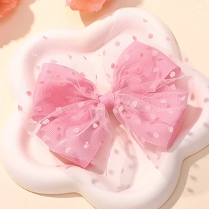 Detailed view of a pink mesh bow hair clip with white polka dots on a petal tray