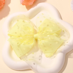 Detail of a yellow mesh bow hair clip with polka dots on a white petal-shaped tray