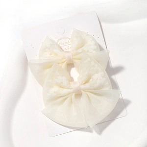 Détail de deux barrettes à nœud en organza blanc cassé avec ruban délicat sur carte de vente