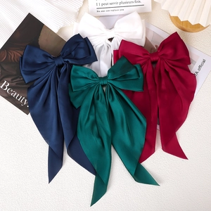 Close-up of four oversized satin bow hair clips in navy, white, green, and burgundy