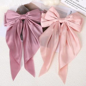 Detailed view of large satin bow hair clips in mauve and pink on a textured surface