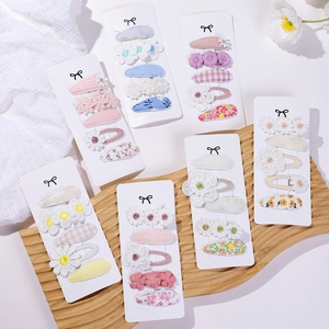 Floral and checkered fabric hair clip sets for girls displayed on a wooden tray