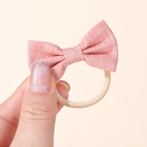 Detailed close-up of a pink fabric bow hair tie with high-elastic beige band for babies