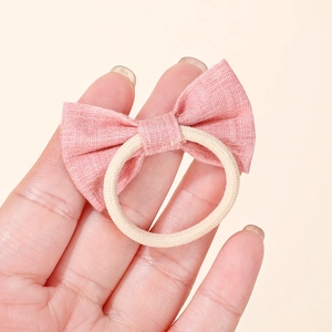 Close-up of a pink fabric bow hair tie showing the detailed cotton linen texture