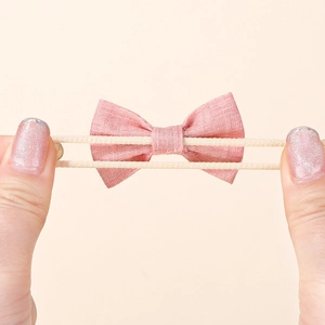 Close-up of pink linen bow hair tie showing elastic band stretch and soft texture