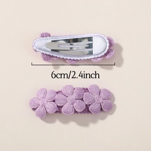 Dettaglio di due fermagli per capelli con fiori ricamati viola e indicazione taglia 6 cm