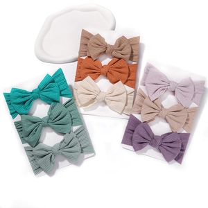 Detailed view of nine elastic ribbed baby headbands with bows in assorted soft colors