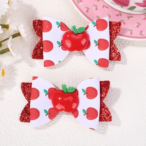Close-up of glittery red apple bow hair clips for kids on a white floral background