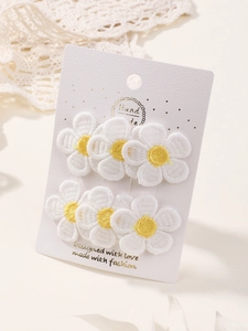 Detailed macro view of four embroidered daisy fabric hair clips on a decorative card
