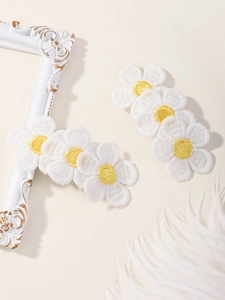 Detail of white embroidered daisy hair clips with yellow centers and fine knit texture