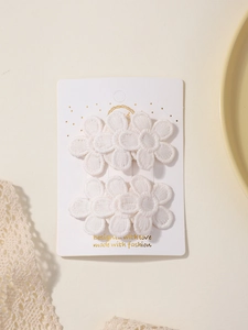 Detailed view of two white lace flower hair clips on a branded display card