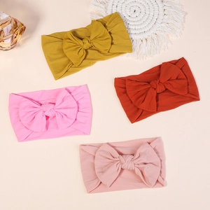 Flat lay of baby nylon bow headbands in mustard, burnt orange, and pink colors