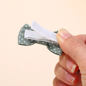 Close-up of a green polka dot bow hair clip with white ribbon-wrapped metal alligator clip