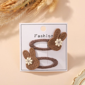 Detail of two handmade brown embroidered bunny hair clips on a Fashion display card