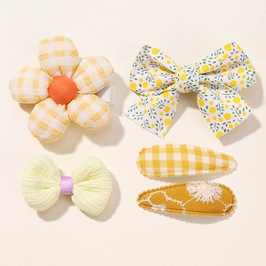 Detailed view of a 5-piece yellow fabric hair clip set with floral bows and grid patterns