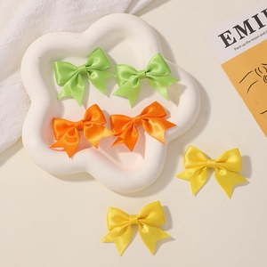 Detailed view of handmade satin bow clips in orange and yellow on a ceramic dish