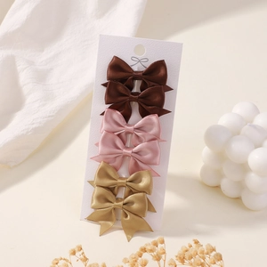 Detailed view of six mini satin bow hair clips in brown, pink, and gold on white card