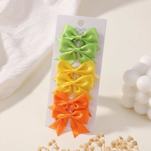 Detail view of 6-piece mini satin bow hair clips in green, yellow, and orange on card