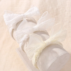 Detail von drei Spitzen-Schleifen-Stirnbändern in Weiß, Creme und Gelb auf Ständer