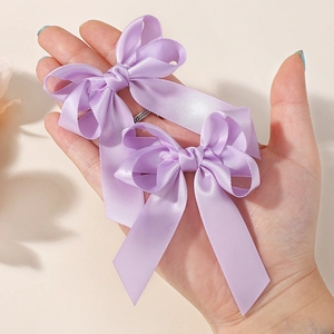 Detail of purple satin double-layer hair bows with long ribbons held by hand