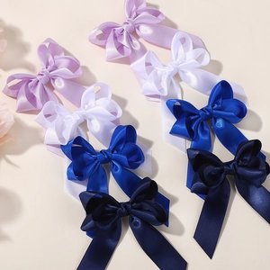 Detail view of handmade satin hair bow clips in purple, blue and white on beige background