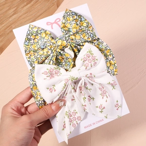 Détail de barrettes à nœud floral en rose et vert présentées sur une carte de support