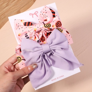 Détails des barrettes à gros nœuds rose à motif bonbon et satin violet sur carte