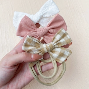 Detailed macro view of three nylon baby headbands featuring lace, solid pink, and plaid bows