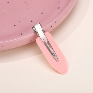 Detailed macro view of a matte pink duckbill hair clip on a decorative pastel ceramic plate