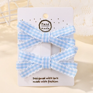Détail de deux barrettes à nœuds en vichy bleu avec bords à volants sur carton