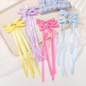 Dettaglio di quattro fiocchi per capelli in raso colorato con lunghe nappe su vassoio