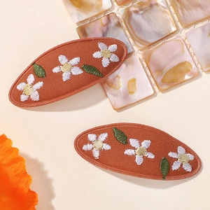 Détail de barrettes en tissu orange avec broderies de fleurs blanches et de feuilles