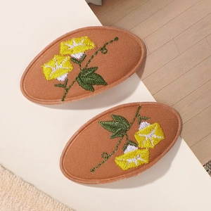 Détail de motifs floraux brodés sur barrettes à cheveux ovales en tissu marron pour fille