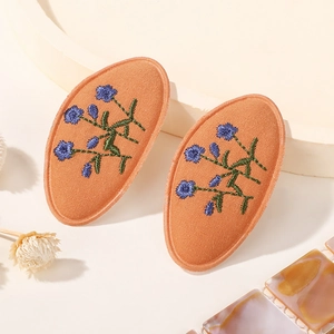 Vue détaillée de pinces à cheveux orange en tissu avec broderie florale bleue raffinée