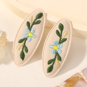 Détail de barrettes ovales en tissu avec broderie florale bleue délicate sur lin beige