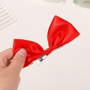 Close-up of red ribbon bow hair clip with silver metal alligator grip and satin texture