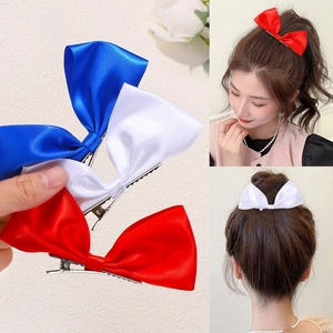 Close-up of three satin bow hair clips in red, blue, and white with metal duckbill clips