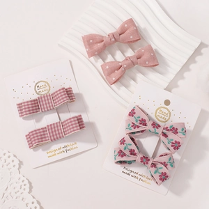 Haarspangen-Set mit rosa Schleifen, Blumenmustern und Karos auf weißer Karte