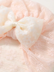 Détail d'un bandeau bébé en dentelle rose avec nœud en tulle et petites perles blanches