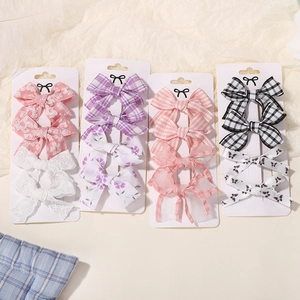 Detailed view of four sets of fabric bow hair clips displayed on white cardboards