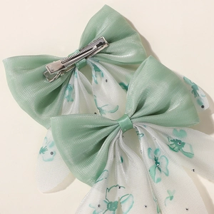 Détail des barrettes nœuds en tulle double épaisseur avec motifs floraux verts et pince crocodile