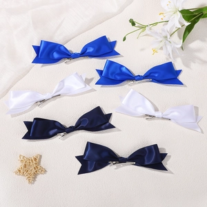 Detail von sechs Satin-Bogen-Haarspangen in Königsblau, Weiß und Marine auf strukturierter Fläche