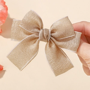 Close-up of champagne gold glitter fabric bow hair clip with white stitched edges